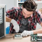 Technicien informatique avec lunettes de protection réparant une carte mère, précision requise similaire à l'entretien d'un TerraMaster U4-500