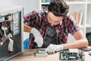 Technicien informatique avec lunettes de protection réparant une carte mère, précision requise similaire à l'entretien d'un TerraMaster U4-500