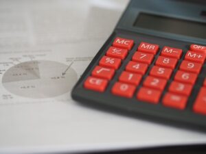 Calculatrice aux touches rouges posée sur des documents financiers avec graphique circulaire visible
