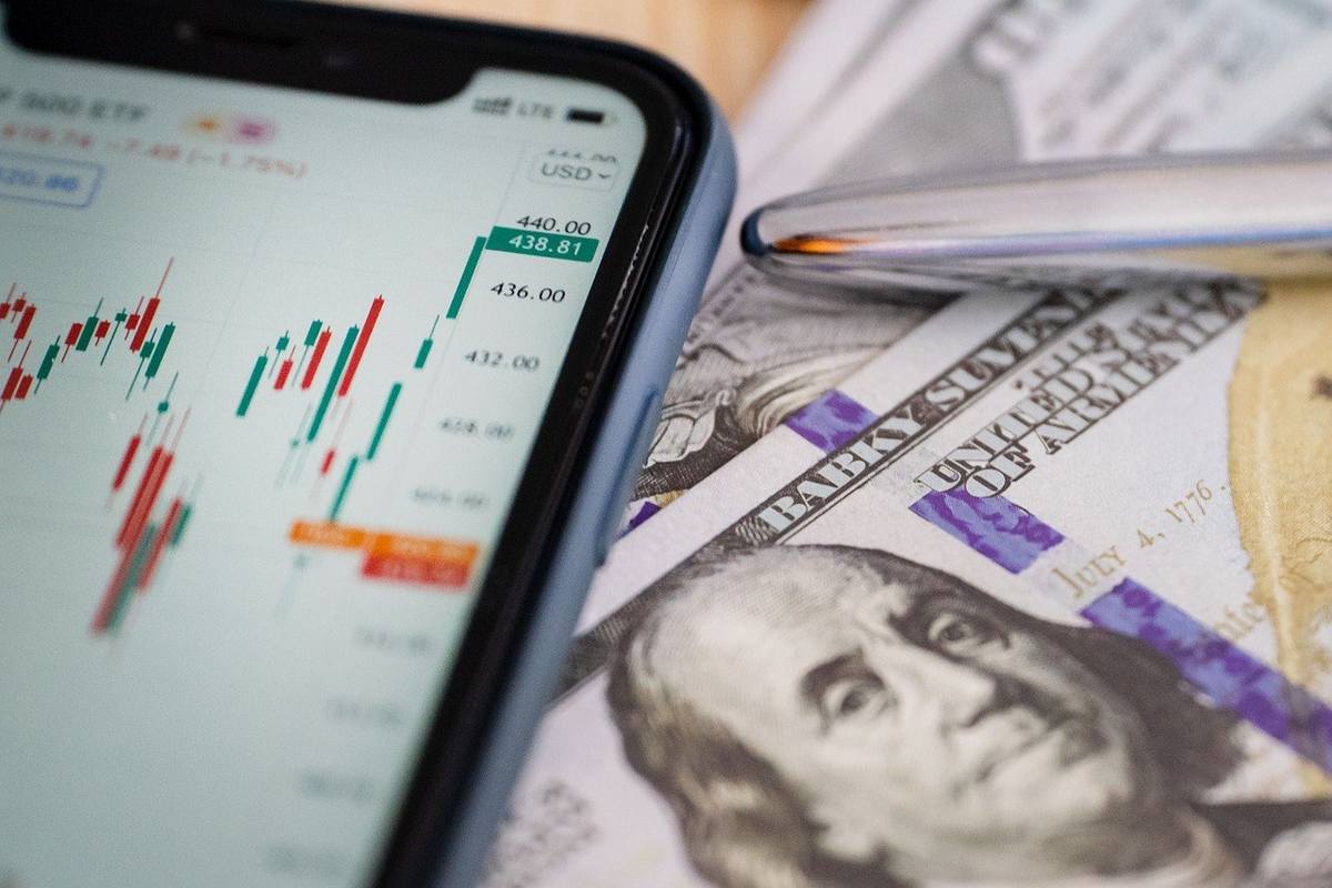 Smartphone montre graphique boursier, stylo et billets de 100 dollars