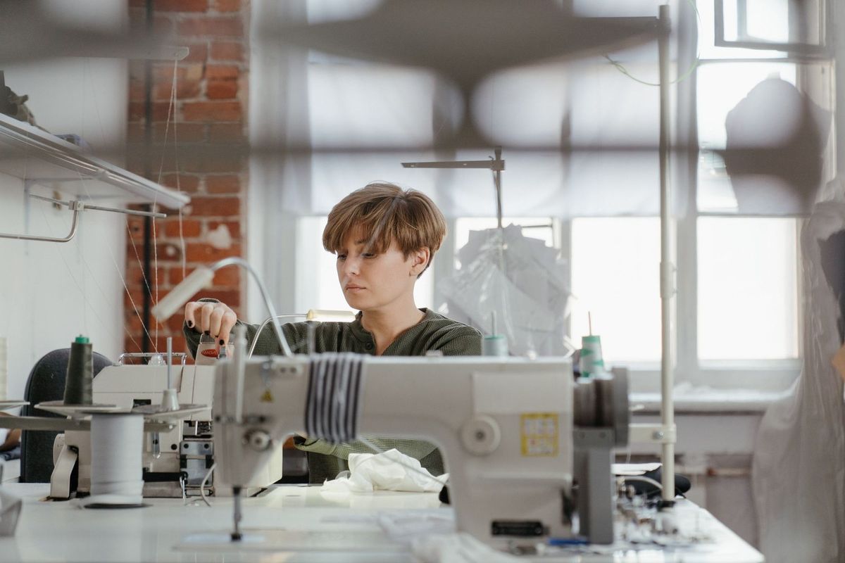 Jeune individu utilisant une machine à coudre dans un atelier lumineux Jeune individu utilisant une machine à coudre dans un atelier lumineux