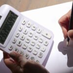 Une main utilise une calculatrice tandis que l'autre écrit sur un papier blanc