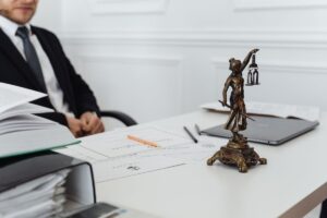 Homme en costume assis à un bureau avec une statue de la justice, des papiers et un ordinateur portable