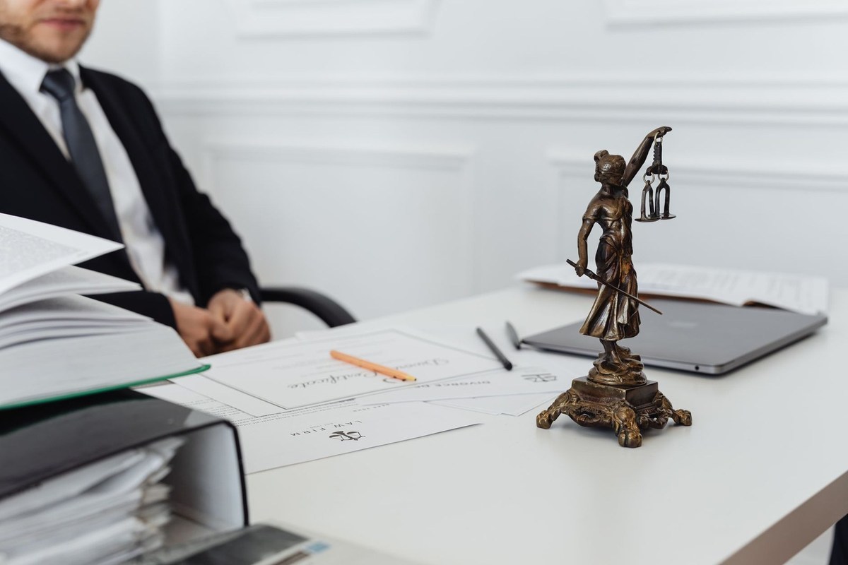 Homme en costume assis à un bureau avec une statue de la justice, des papiers et un ordinateur portable Homme en costume assis à un bureau avec une statue de la justice, des papiers et un ordinateur portable