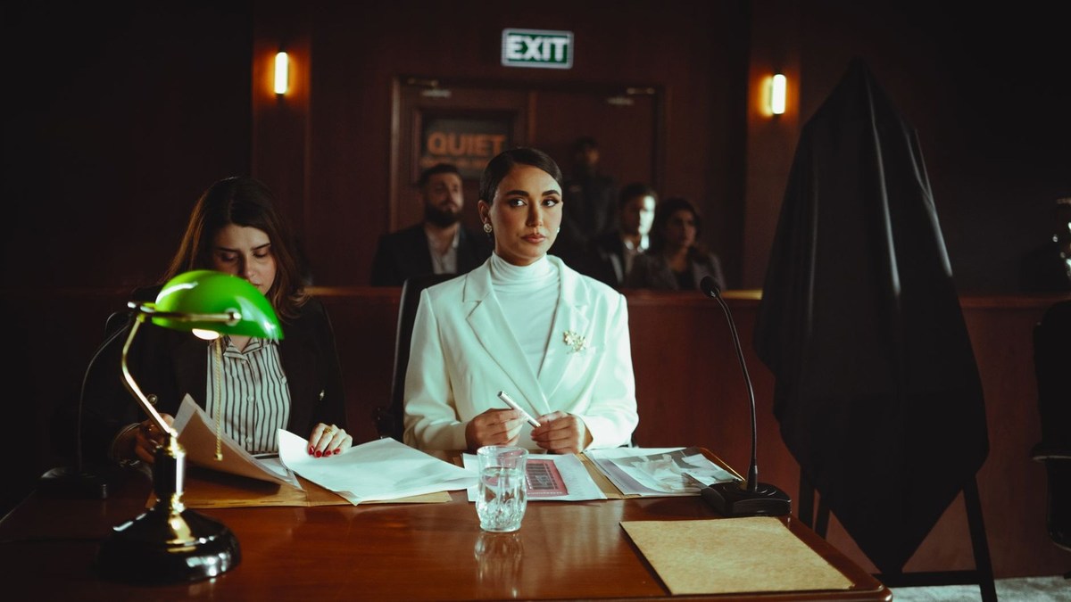 Femme en blouse devant documents, lampe verte, tribunal, autres personnes Femme en blouse devant documents, lampe verte, tribunal, autres personnes