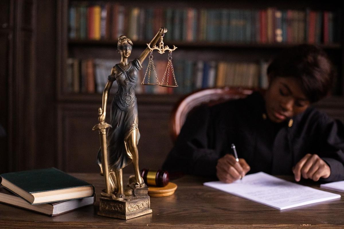 Statue de la justice, gavel, livres, personne écrivant dans une bibliothèque Statue de la justice, gavel, livres, personne écrivant dans une bibliothèque