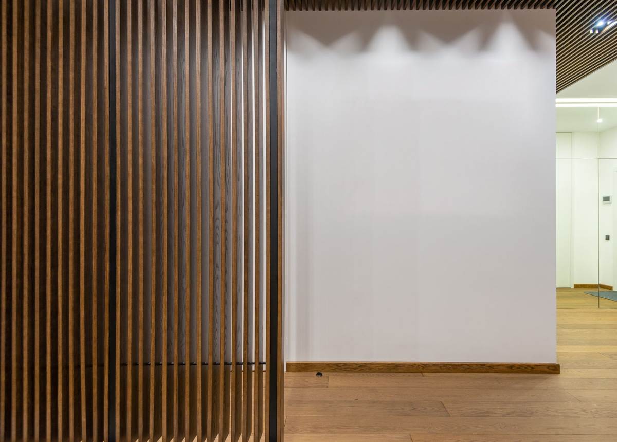 Vue d'un couloir avec paroi en bois ajouré et mur blanc