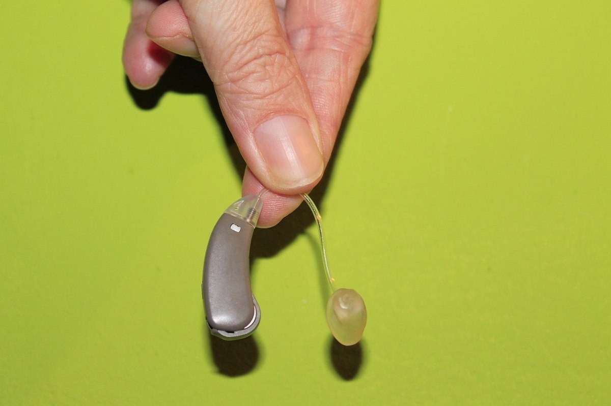 Main présentant un appareil auditif contour d'oreille gris avec tube auriculaire transparent sur fond jaune