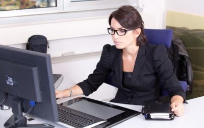 Une femme en costume noir travaille sur son ordinateur de bureau