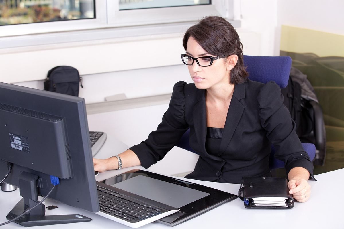 Une femme en costume noir travaille sur son ordinateur de bureau